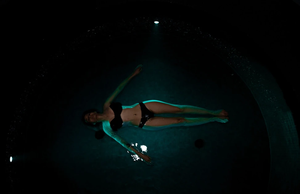 A person floats in a dimly lit pool, creating a serene and relaxing atmosphere, emphasizing relaxation at Wellnesshotel Klosterhof.