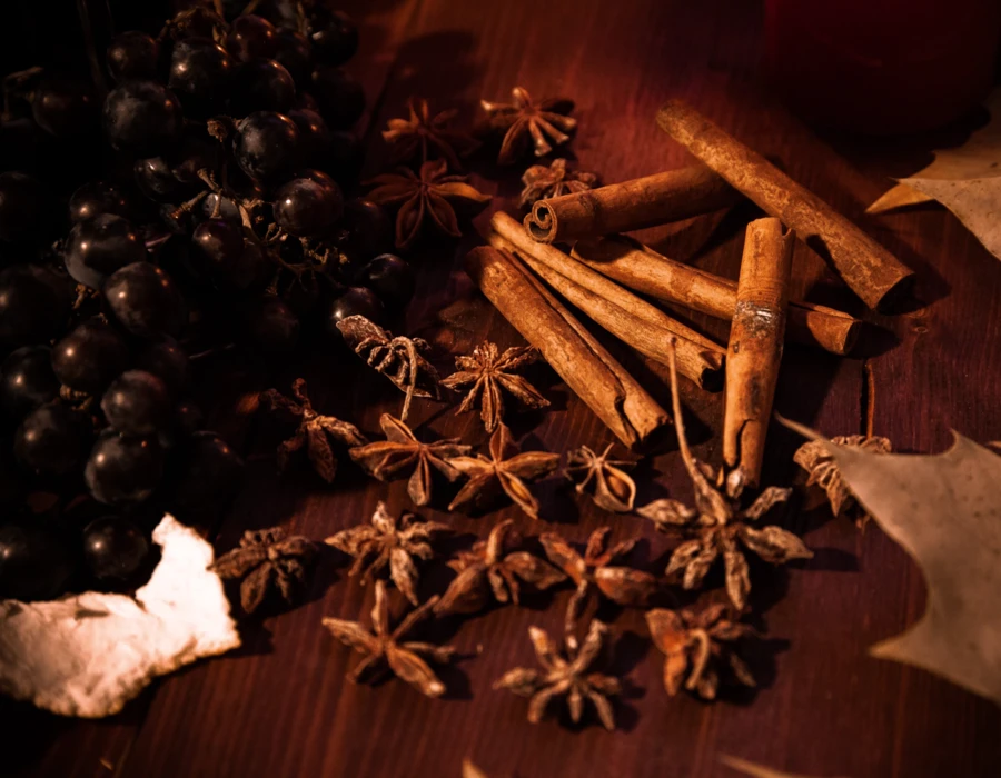 Zimtstangen, Sterneanis und Trauben auf einem Holztisch, umgeben von getrockneten Blättern und einer warmen Atmosphäre.
