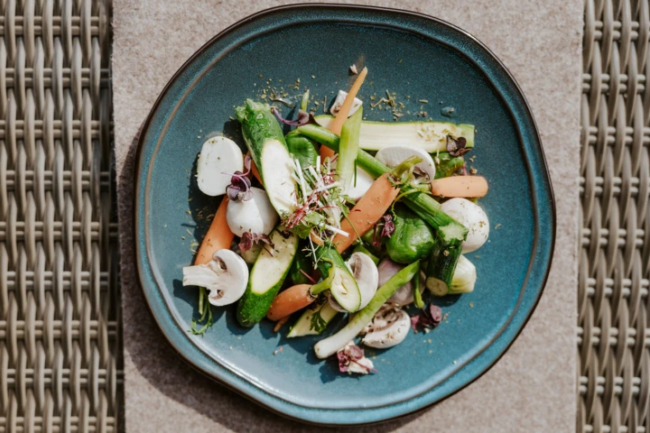 A colorful plate of fresh vegetables elegantly arranged on a blue dish, served at Hotel Klosterhof.