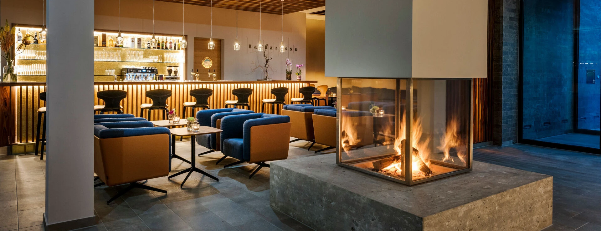 Modern lounge with a cozy fireplace at Hotel Klosterhof. Comfortable seating and a well-stocked bar create a welcoming atmosphere.