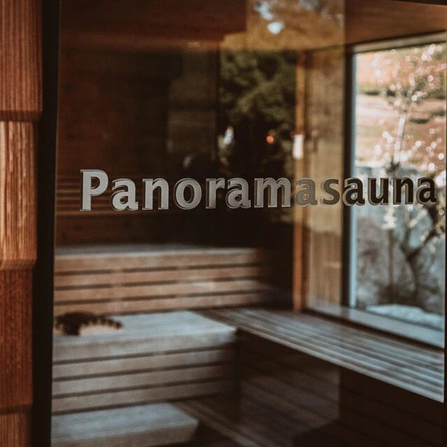 Glasierte Tür mit dem Schriftzug "Panoramasauna", Blick auf die Holzbank im Innenraum des Wellnessbereichs.