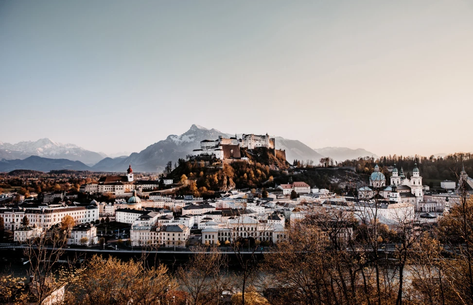 Salzburgs Altstadt mit Festung Hohensalzburg im Hintergrund, umgeben von Bergen und Fluss, bei Sonnenuntergang.