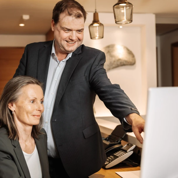 Ein Mann und eine Frau sitzen am Schreibtisch und betrachten gemeinsam einen Computerbildschirm im Hotel Klosterhof.
