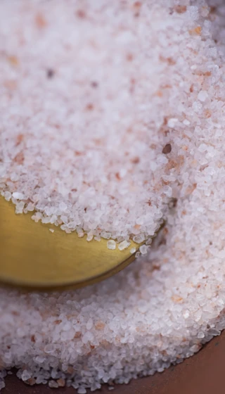 Nahaufnahme von Himalaya-Salz in einem Gefäß mit einem goldenen Löffel, perfekt für Wellness im Hotel Klosterhof.