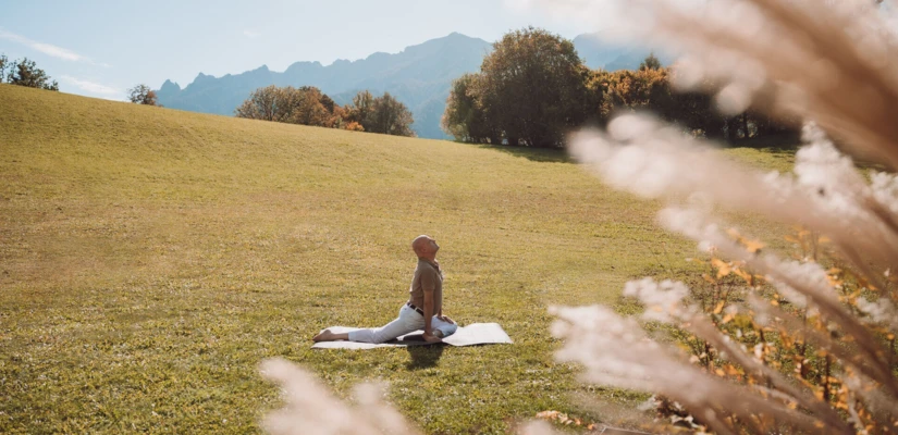 A person practices yoga in a serene meadow at Wellnesshotel Klosterhof, surrounded by autumn trees and distant mountains.
