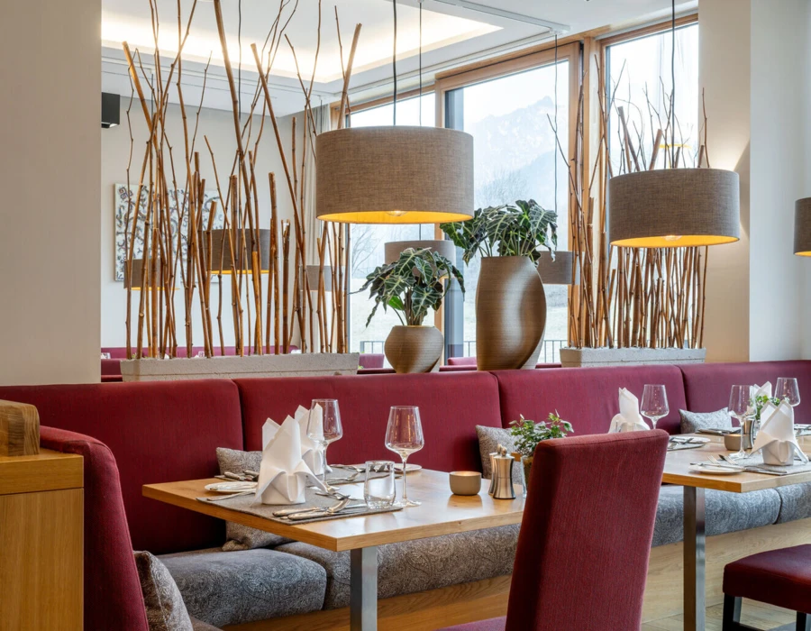 Gemütliche Restaurantatmosphäre im Hotel Klosterhof mit roten Sitzbänken, eleganten Tischen und Blick auf die bayerischen Alpen.