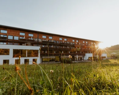 Moderne Fassade des Hotel Klosterhof in Bayerisch Gmain, umgeben von Wiese und Alpen bei Sonnenuntergang. Wellnesshotel mit alpinem Charme.