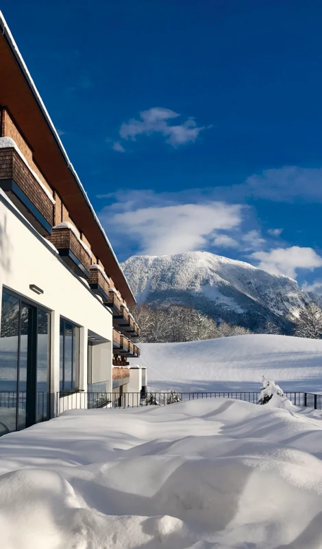 Schneebedeckte Landschaft mit Blick auf die Berge und das Hotel Klosterhof in Bayerisch Gmain. Helle, sonnige Atmosphäre.