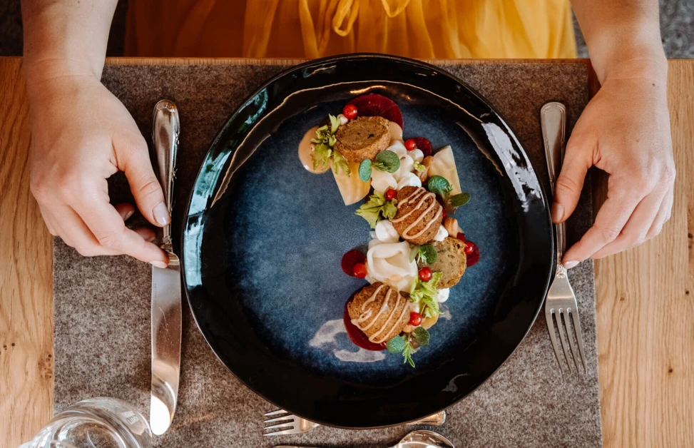 A gourmet dish elegantly presented on a dark plate, with vibrant garnishes, on a wooden table setting.