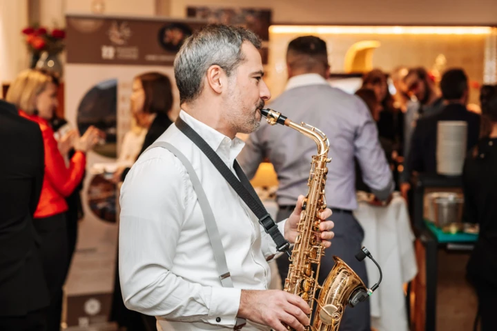 Ein Saxophonist spielt auf einer Veranstaltung im Hotel Klosterhof, umgeben von G&auml;sten in festlicher Stimmung.