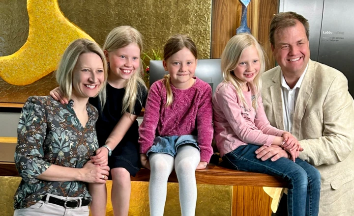 Familie posiert l&auml;chelnd vor goldener Wand, umgeben von Kindern und Erwachsenen in freundlicher Atmosph&auml;re.