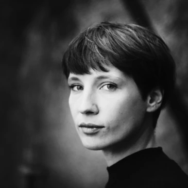 Schwarzweiß-Porträt einer Person mit kurzem Haar, die über die Schulter blickt.