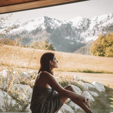 Eine Frau sitzt entspannt am Fenster und blickt auf die majestätischen Berge und die grüne Wiese im Klosterhof.
