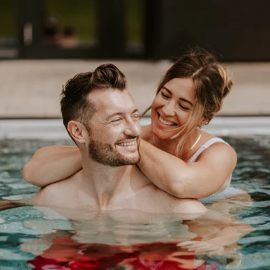 Couple smiling in a pool at Wellnesshotel Klosterhof in Bayern, enjoying a relaxing moment.