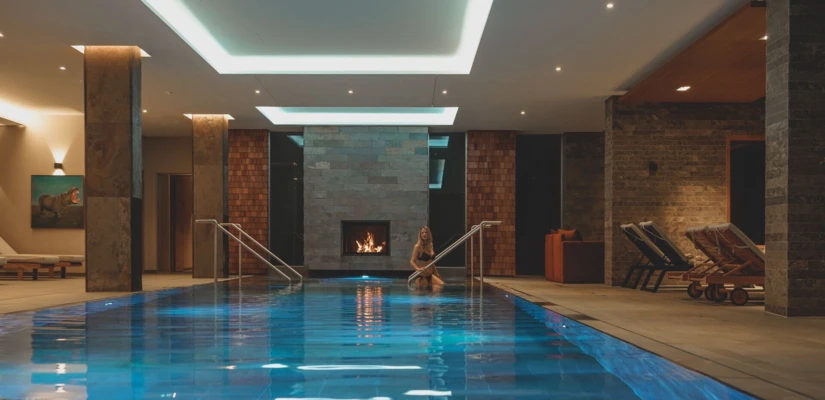 Luxurious indoor pool with a cozy fireplace at Hotel Klosterhof, featuring lounge chairs and ambient lighting.