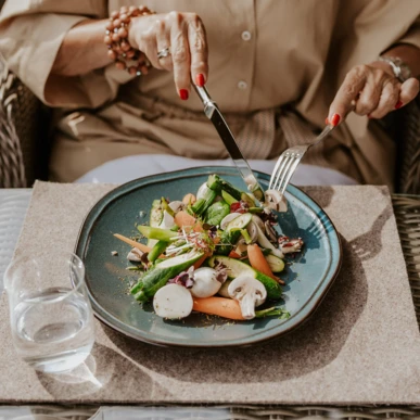 Eine Person schneidet einen bunten Salat auf einem blauen Teller, während ein Glas Wasser daneben steht.