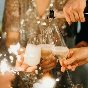 Sekt und Cocktails werden in eleganten Gläsern angestoßen, umgeben von funkelnden Lichtern und festlicher Stimmung.