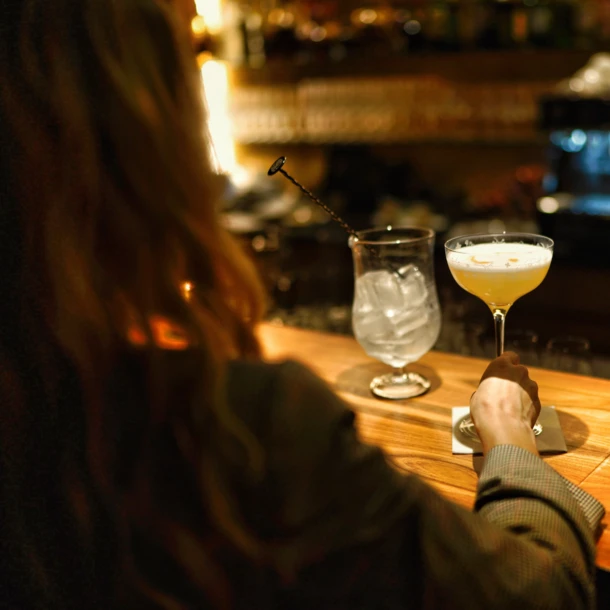A person holding a cocktail glass at a dimly lit bar counter.