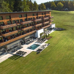 Moderne Hotelansicht mit Terrasse und Liegen, umgeben von gepflegtem Grün und einem kleinen Pool im Vordergrund.