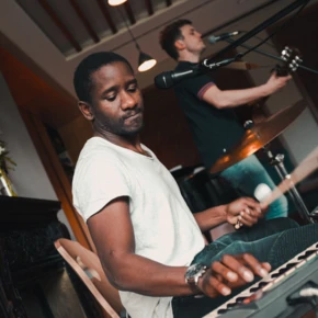 Ein Musiker spielt leidenschaftlich auf einem Keyboard, während ein Kollege im Hintergrund Gitarre spielt.