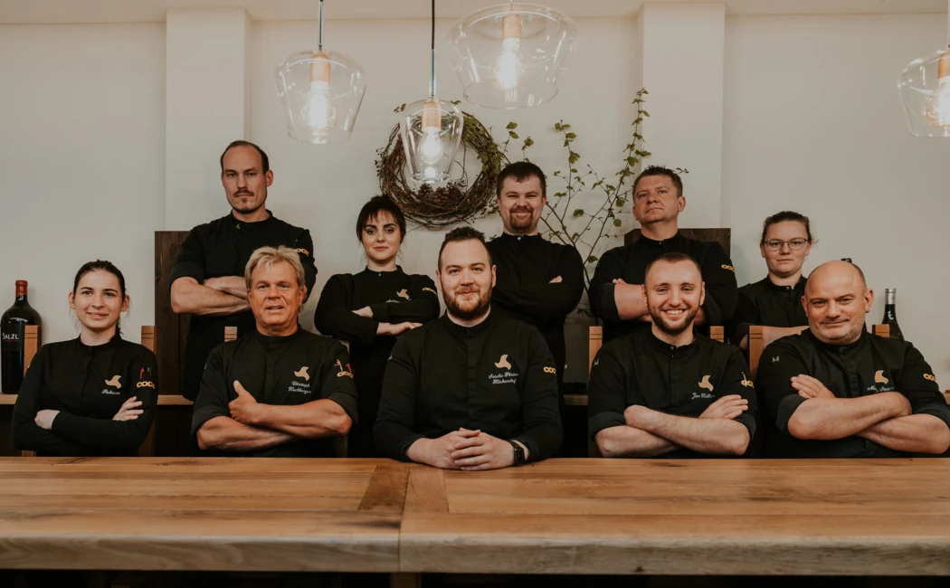 Ein Team von Köchen posiert lächelnd vor einem Holztisch in einem modernen Restaurant.