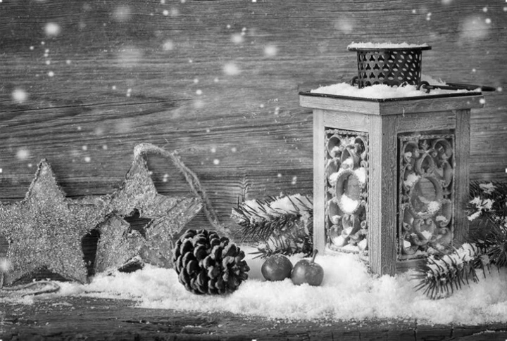 Eine festliche Laterne auf einem holzigen Tisch, umgeben von Tannenzapfen, Sternen und winterlicher Dekoration im Schnee.