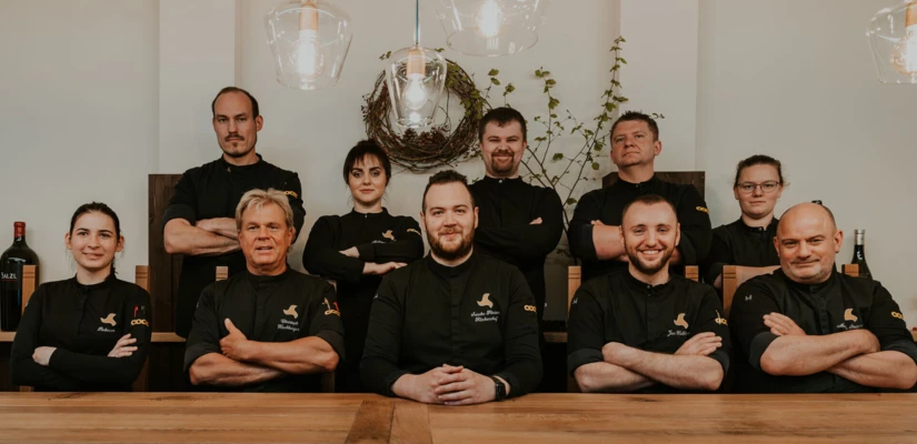 Ein Team von Köchen posiert lächelnd vor einem Holztisch in einem modernen Restaurant.