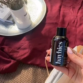 Hand hält eine Flasche "baybies" auf einem roten Untergrund, umgeben von dekorativen Elementen und Geschenken für ein Event.