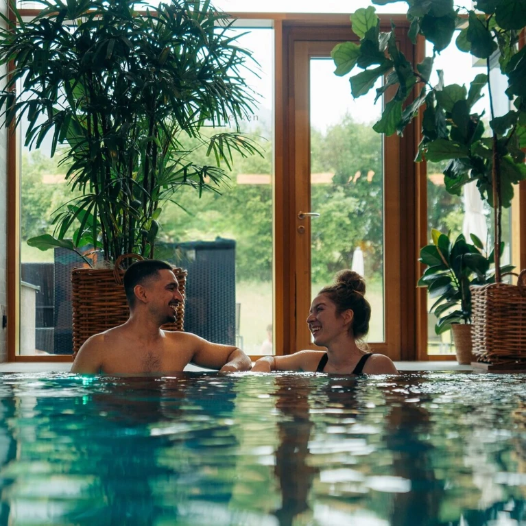 Ein Paar genießt Zeit im Pool des Wellnesshotels Klosterhof, umgeben von Pflanzen und natürlichem Licht.