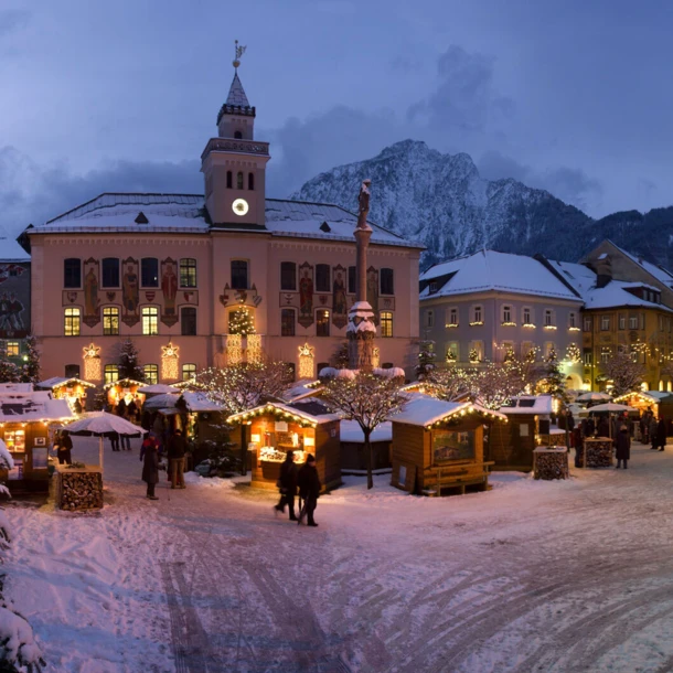 Winterliche Marktszene in Bayerisch Gmain mit festlich beleuchteten Ständen und schneebedeckten Bäumen vor dem Hotel Klosterhof.
