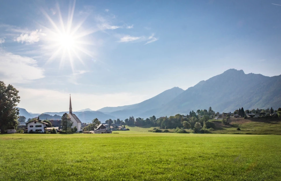 Sonniger Blick auf die Landschaft mit einer Kirche in Bayerisch Gmain, umgeben von Bergen und Wiesen.