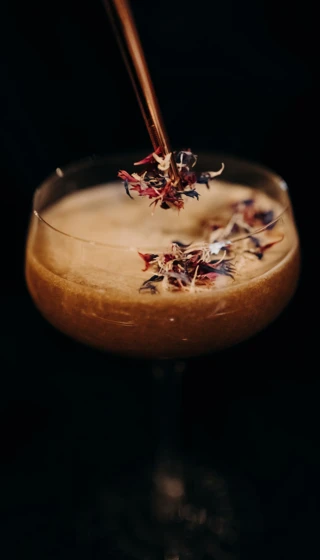 Ein elegantes Cocktailglas mit blühenden Kräutern, serviert im Hotel Klosterhof, einem Wellnesshotel in Bayerisch Gmain.
