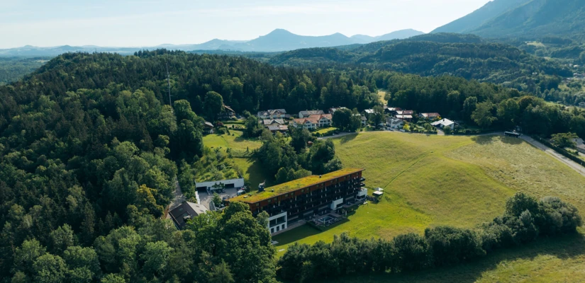 Luftaufnahme eines Hotels inmitten grüner Landschaft, umgeben von Wäldern und sanften Hügeln. Ideal für Erholung und Naturerlebnisse.