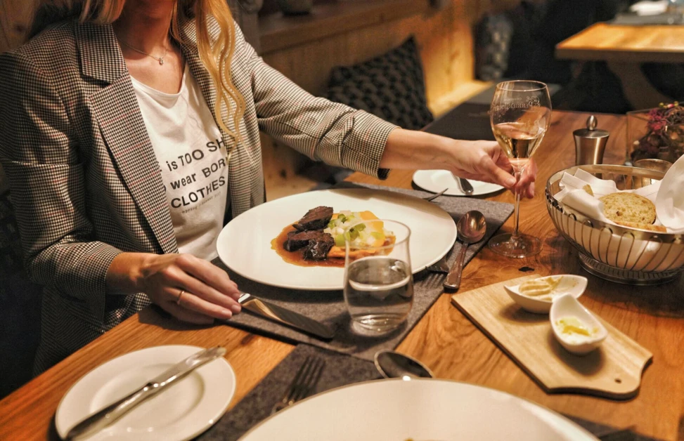 Eine elegante Frau genießt ein Gourmetessen mit Wein in einem stilvollen Restaurant des Hotel Klosterhof in Bayern.