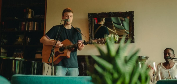Ein Musiker mit Gitarre tritt im Hotel Klosterhof auf, während Gäste in einer gemütlichen Atmosphäre entspannen.