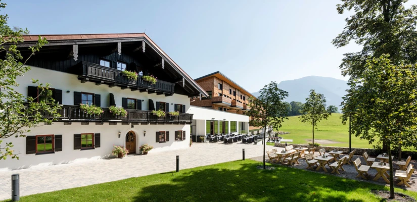Ein malerisches Hotelgebäude mit traditioneller Architektur, umgeben von Grünflächen und gemütlichen Sitzgelegenheiten im Freien.