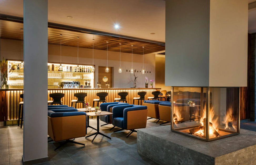 Moderne Hotel-Lounge im Hotel Klosterhof mit zentralem Kamin, eleganten Sitzbereichen und einer stilvollen Bar.