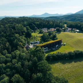 Luftaufnahme eines Hotels inmitten grüner Landschaft, umgeben von Wäldern und sanften Hügeln. Ideal für Erholung und Naturerlebnisse.