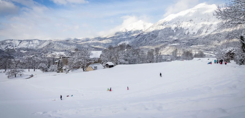 Schneebedeckte Landschaft mit Menschen, die im Schnee spielen; im Hintergrund Berge und eine skandinavische Landschaft.