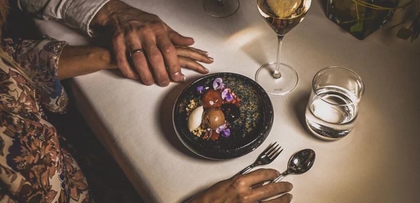 Ein romantisches Abendessen mit zwei Händen, einem Dessert und Gläsern Wein auf einem elegant gedeckten Tisch im Hotel Klosterhof.