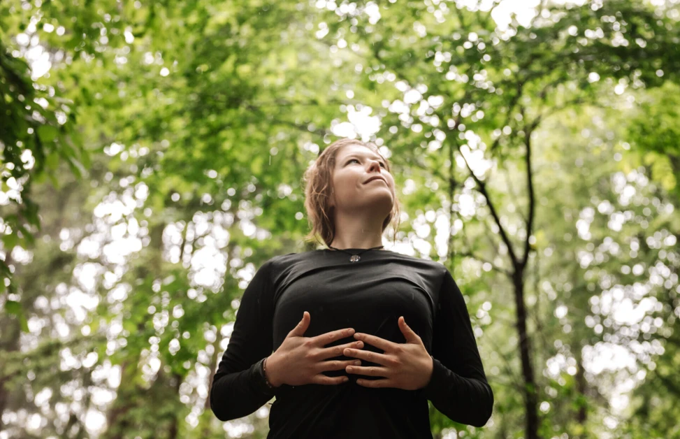 Eine Person steht in einem Wald, schaut nach oben und genießt die Natur um sich herum.