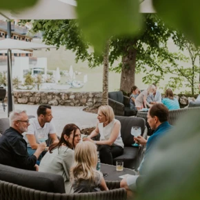Guests relax in an outdoor lounge at Hotel Klosterhof, enjoying drinks and conversation under umbrellas and trees.